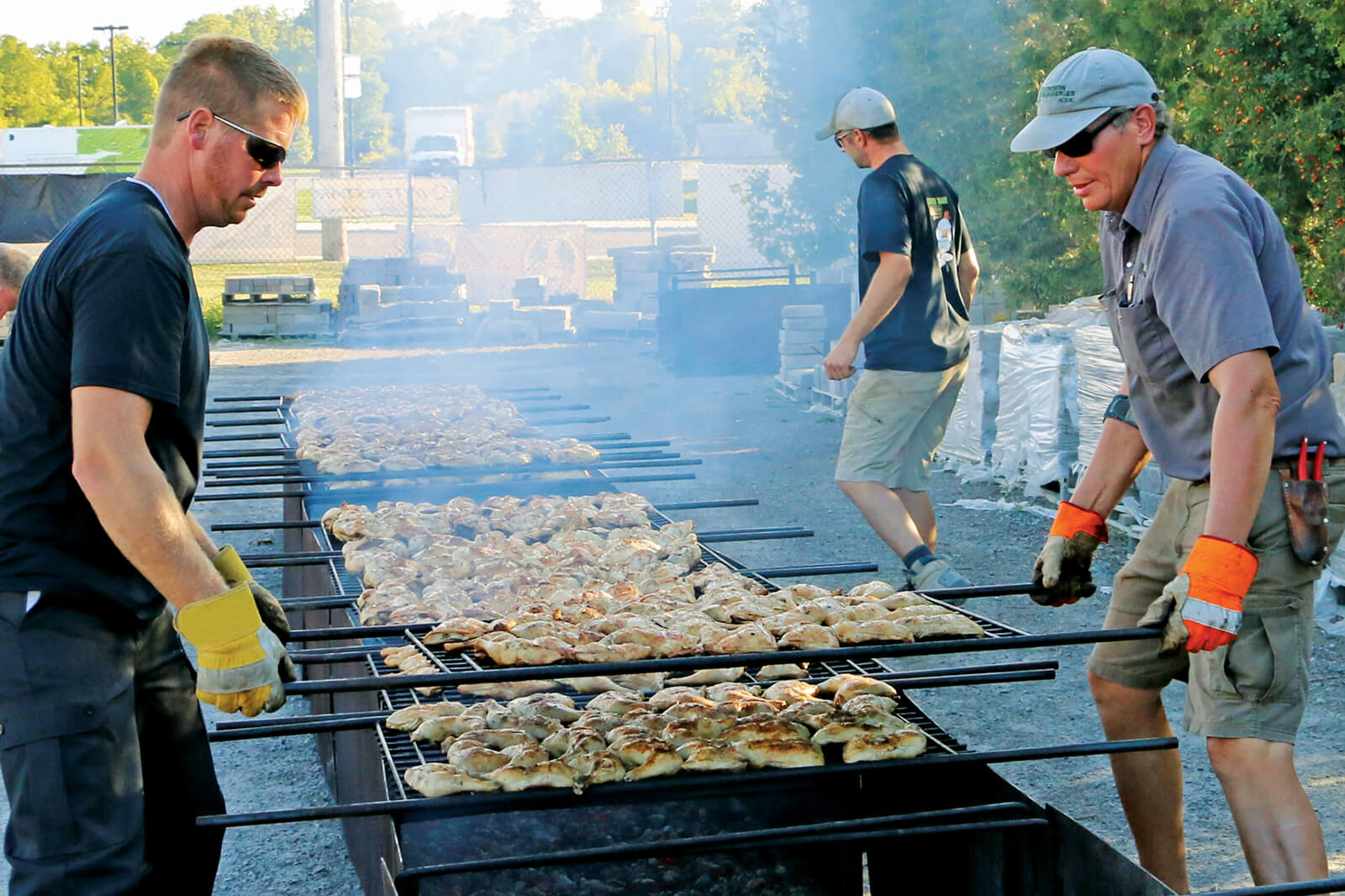 two men cooking chicken on a large barbecue