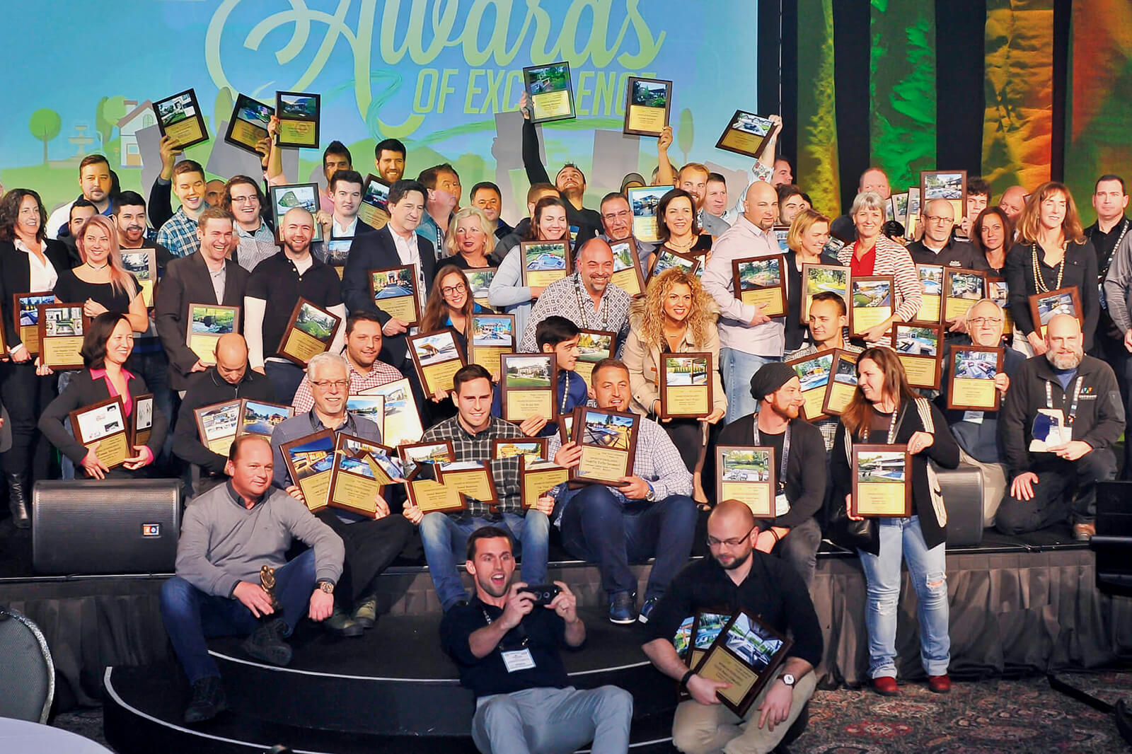 large crowd of people on stage showing off their awards