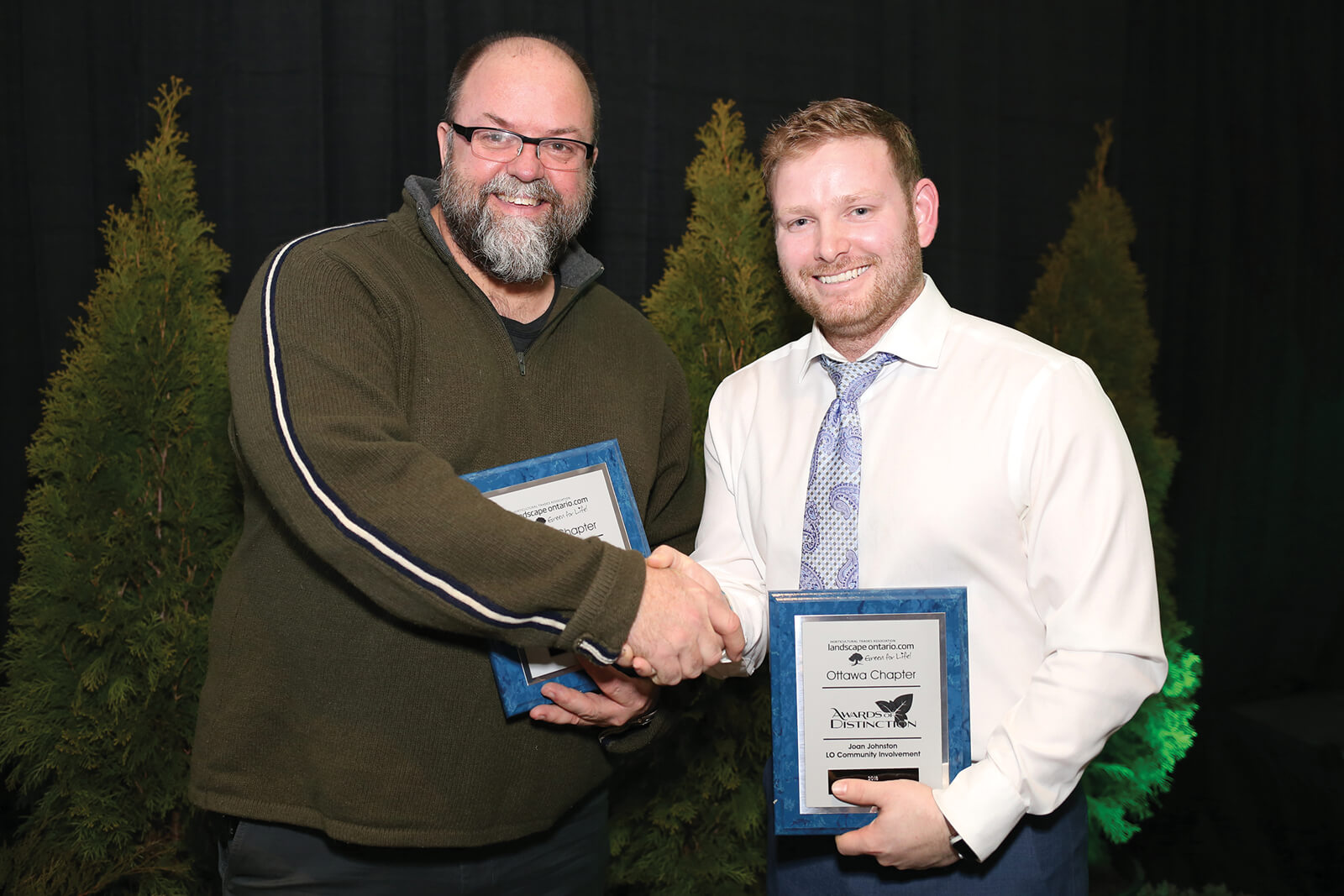 two men shaking hands and holding awards