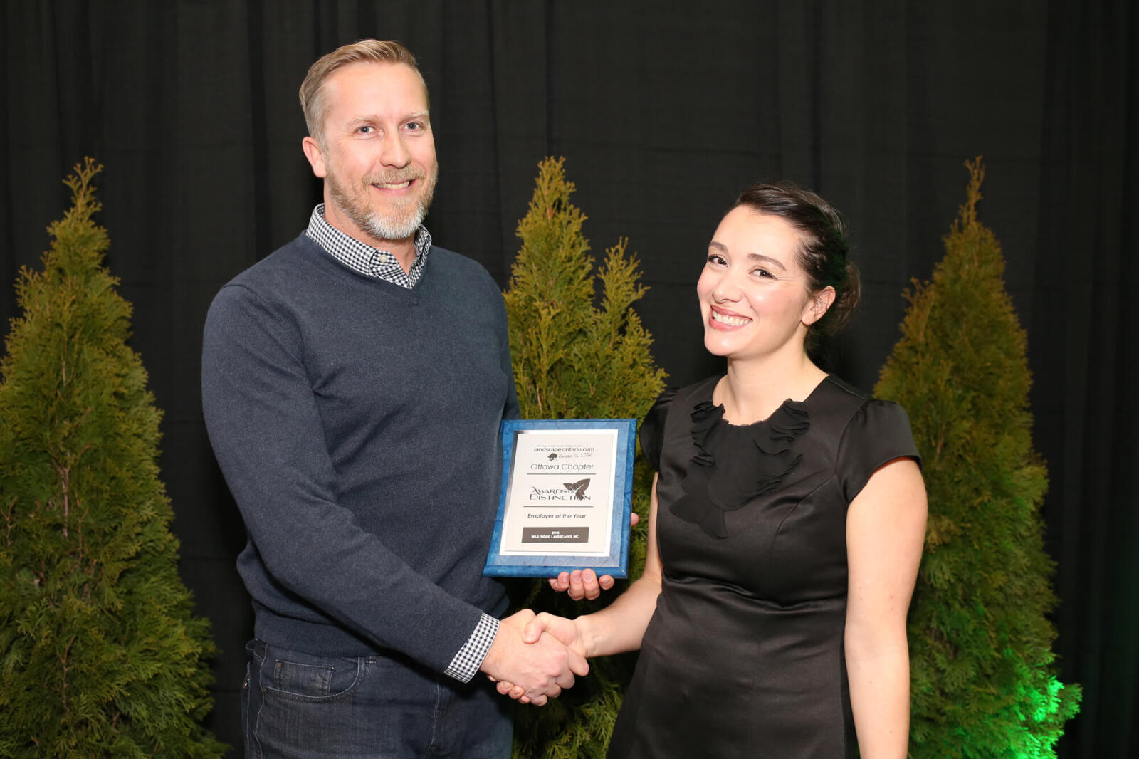 man and woman holding an award plaque and shaking hands