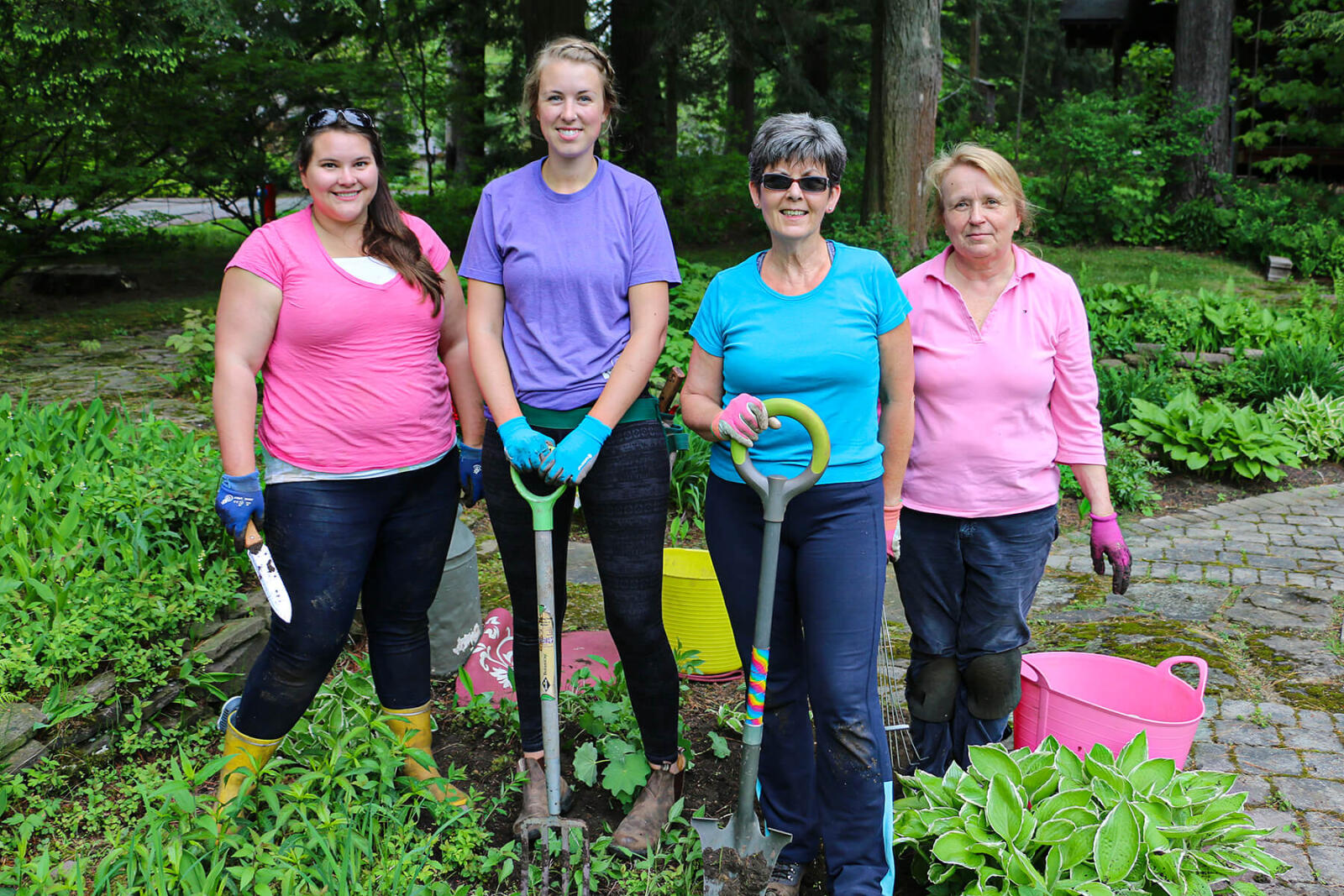 four women with gardening tools take a break from working in the garden
