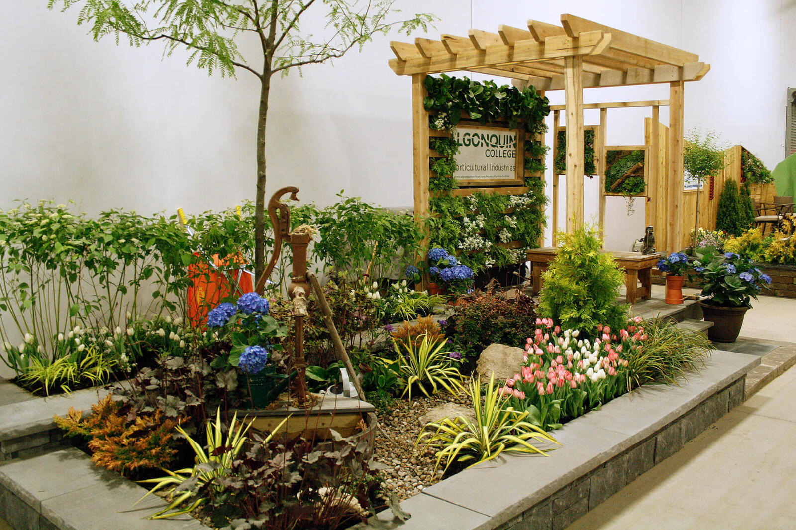 arbor with a green wall and many plants in the foreground