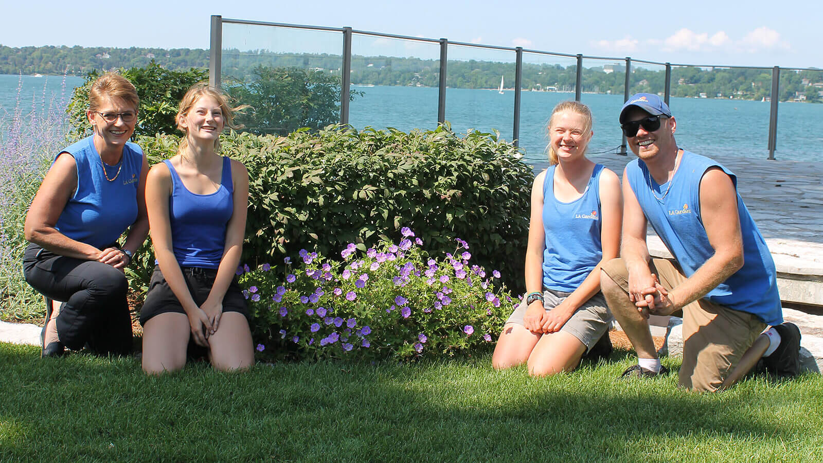 four people kneeling on the grass in front of a lake