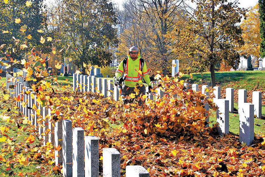 man using leaf blower around headstones