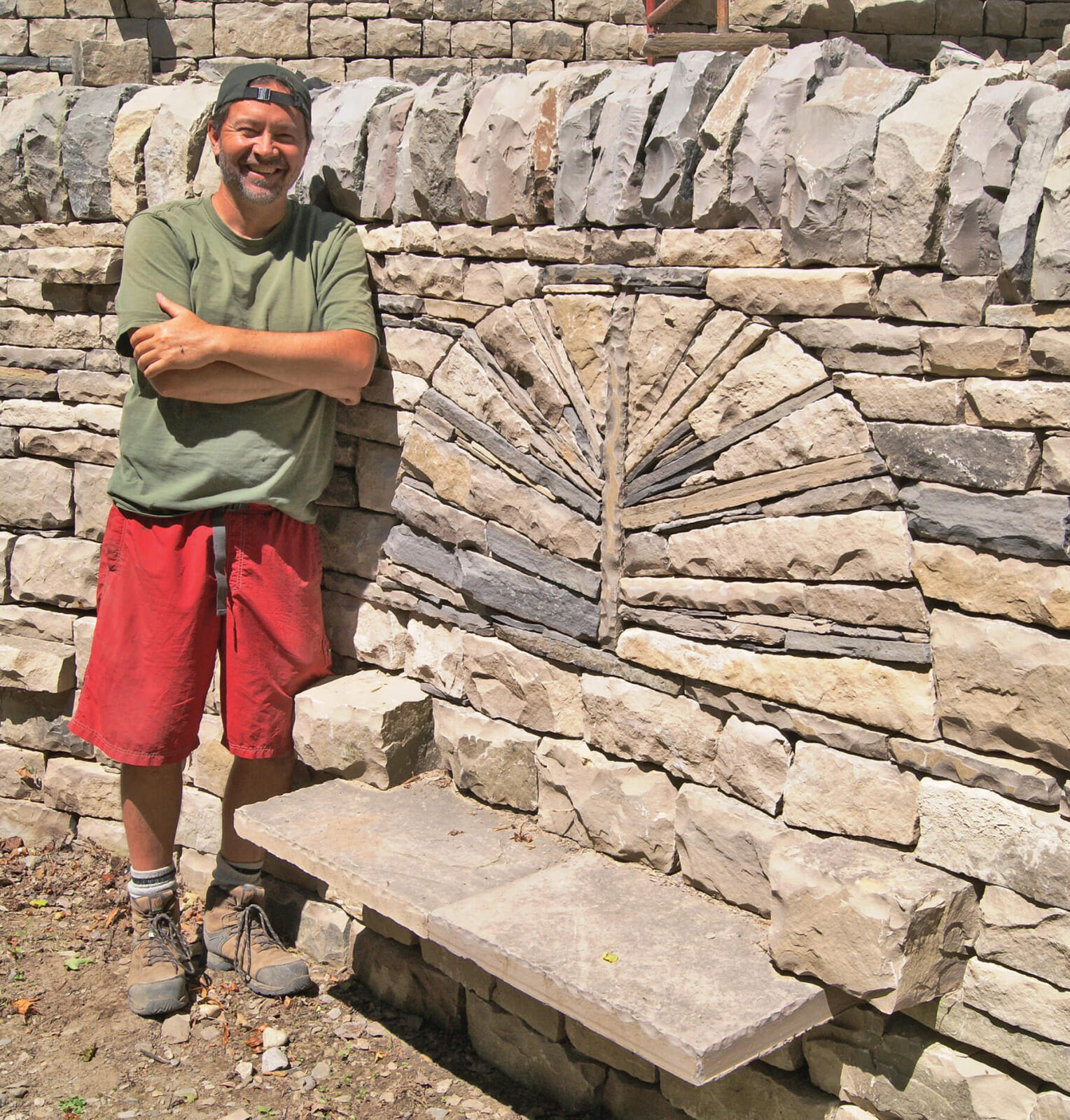 man proudly standing beside a large stone wall with built in bench