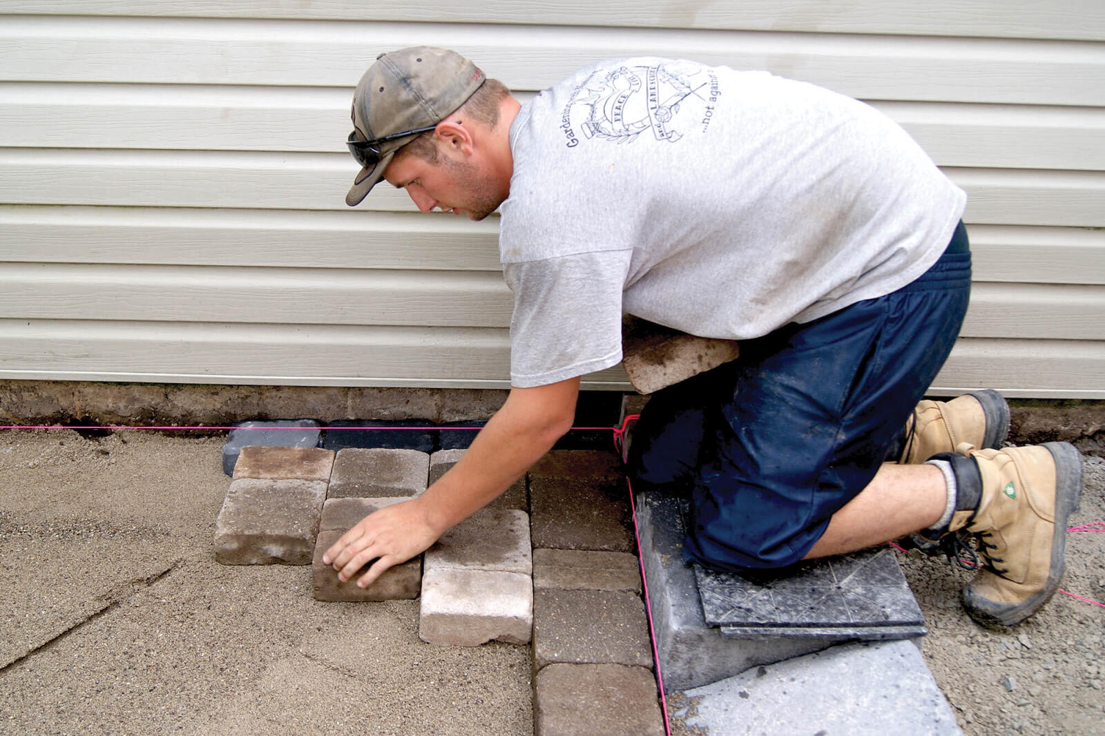 man laving pavers at the side of a house
