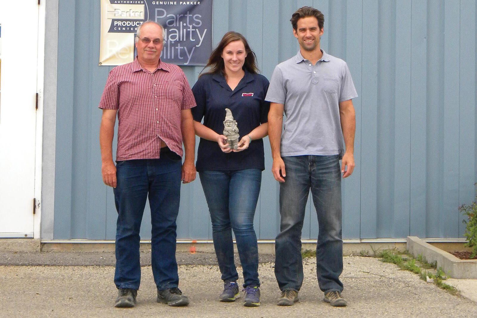 three people posing with a small garden gnome
