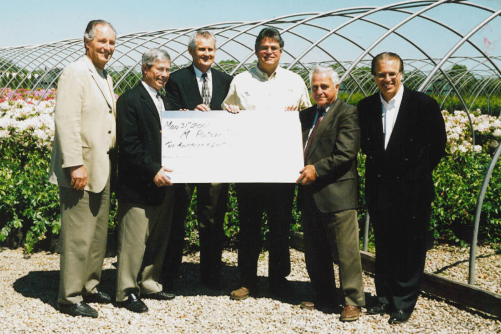 six men holding a cheque in nursery outdoors