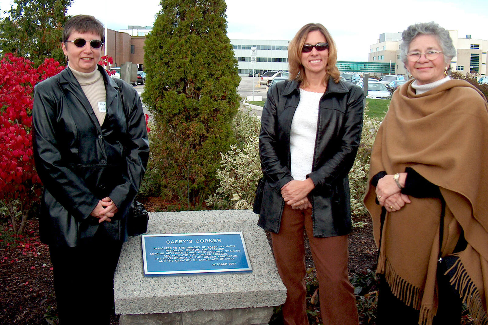 three women standing in a garden with a plaque