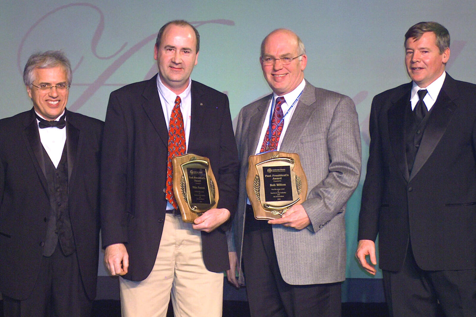 four men on stage, two holding awards