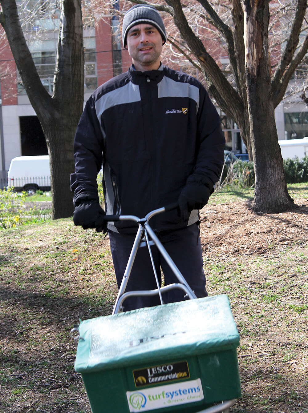 man pushing a seed spreader in a park