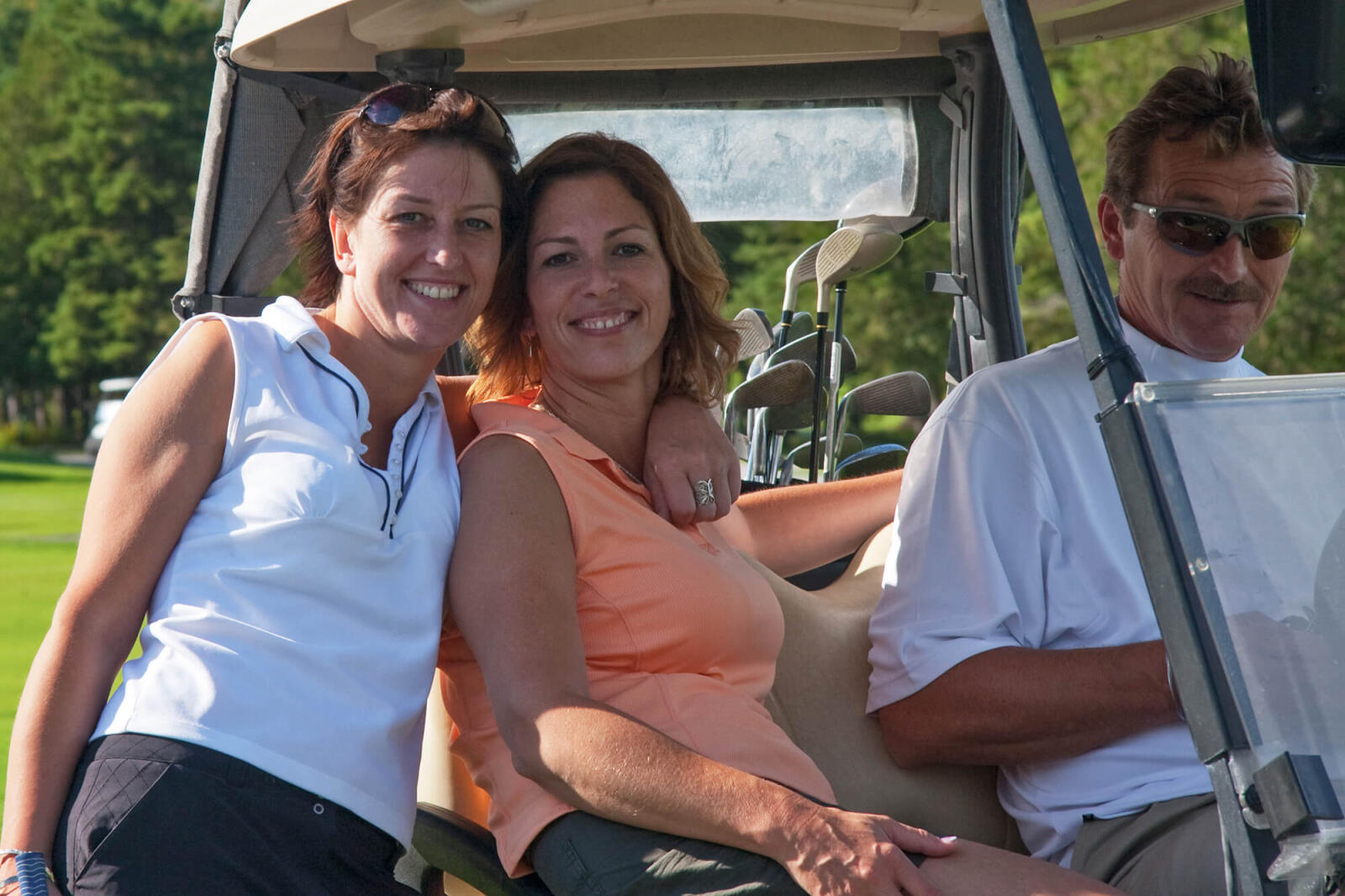 two women and a man in a golf cart