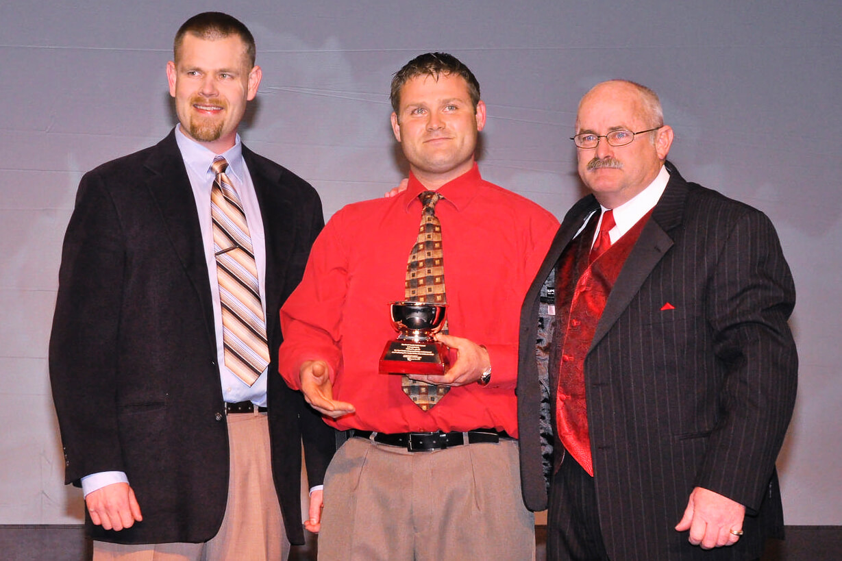 three men one holding an award