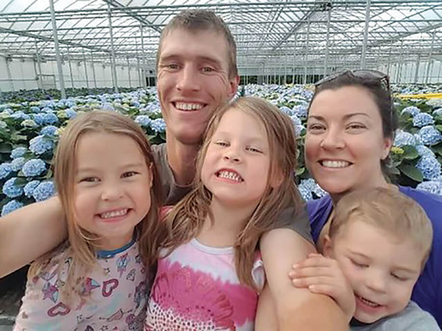 man with wife and three young kids in a greenhouse