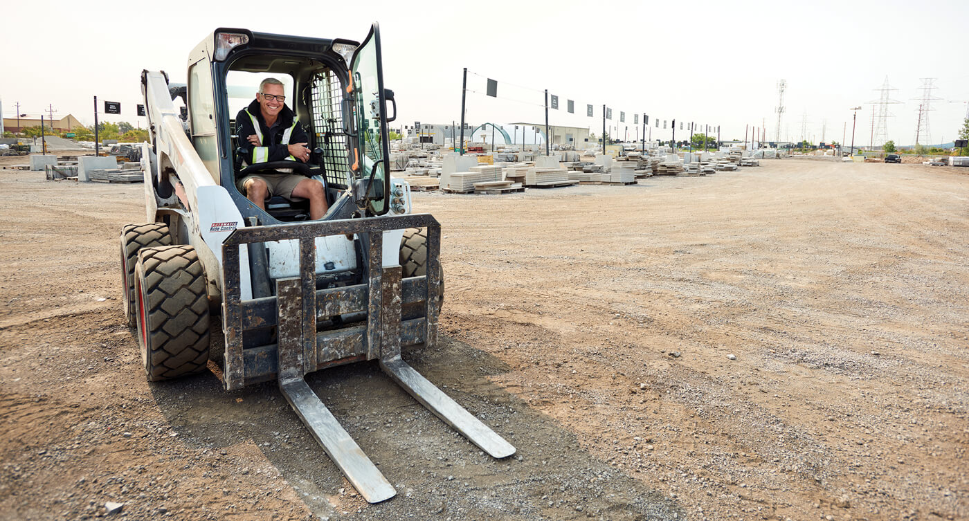 man sitting in a skid steer in a stone yard