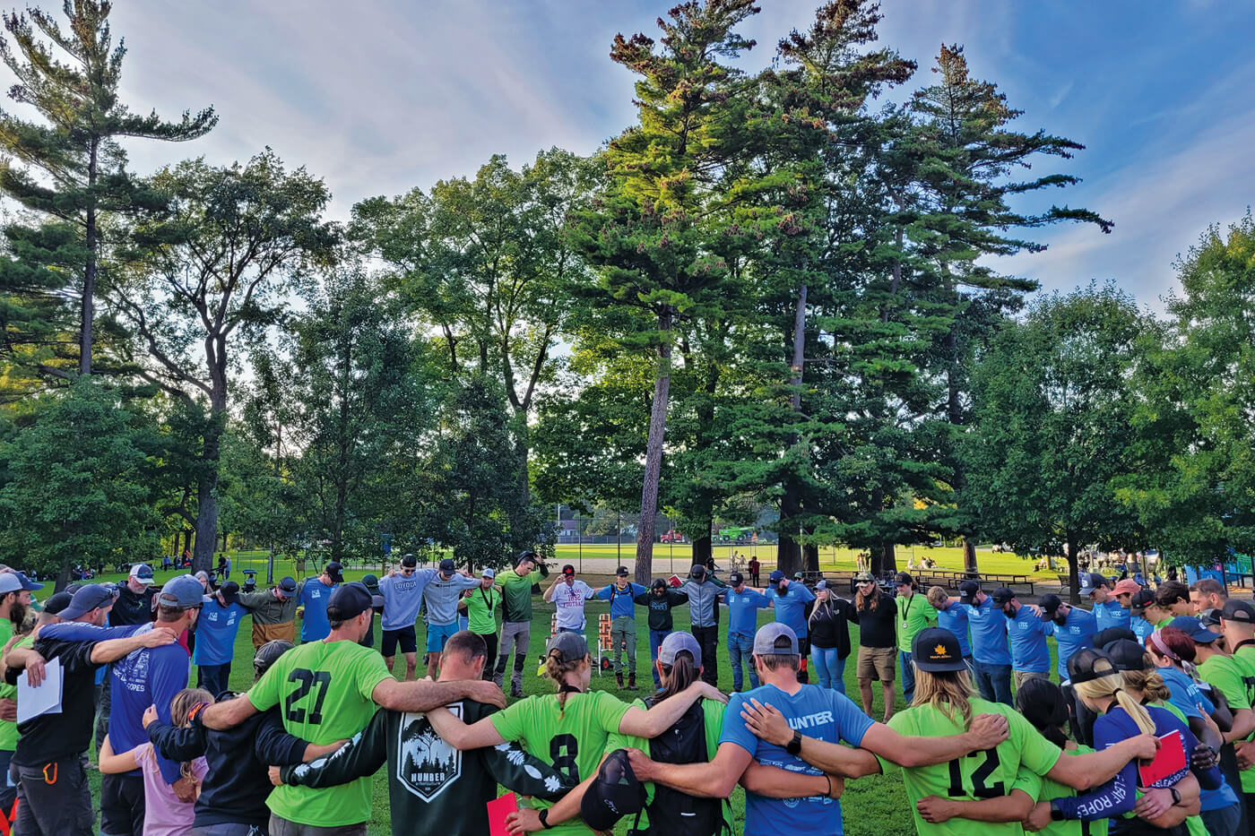 circle of people united in a field overlooked by tall trees