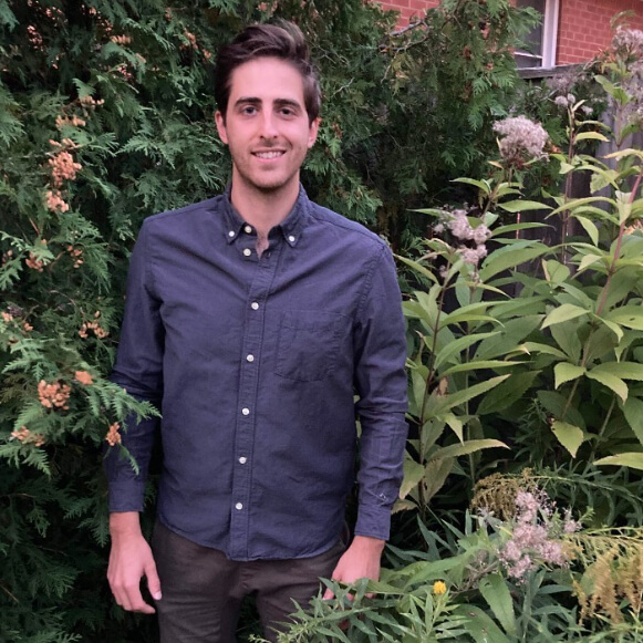 man standing outside in front of a tall shrub