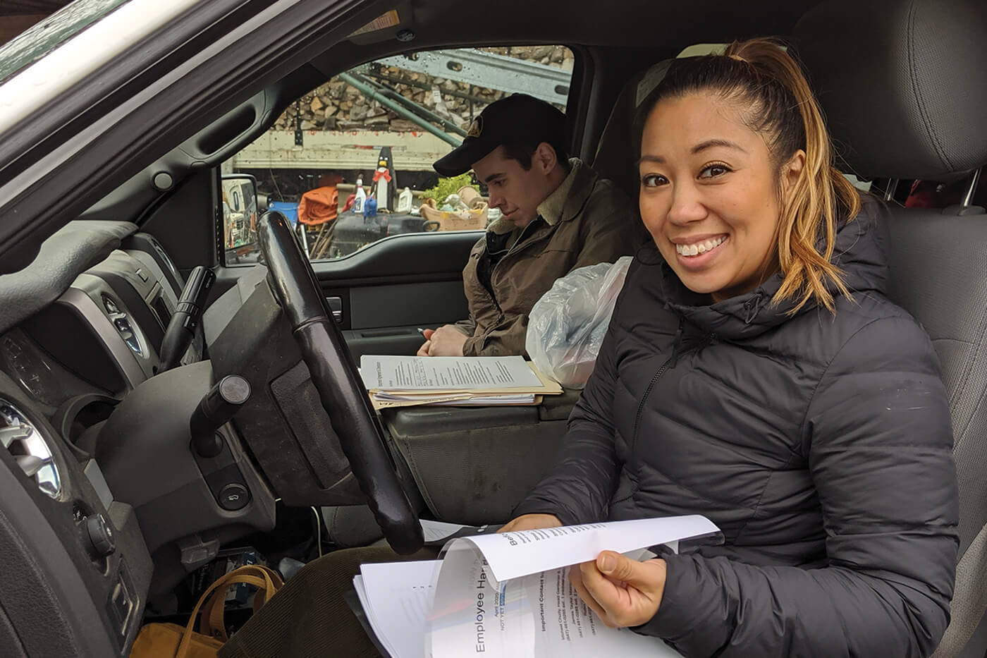 young woman sitting in a vehicle looking at paperwork and smiling