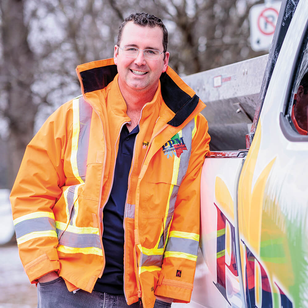 A man in an orange construction vest standing beside a white pick up truck