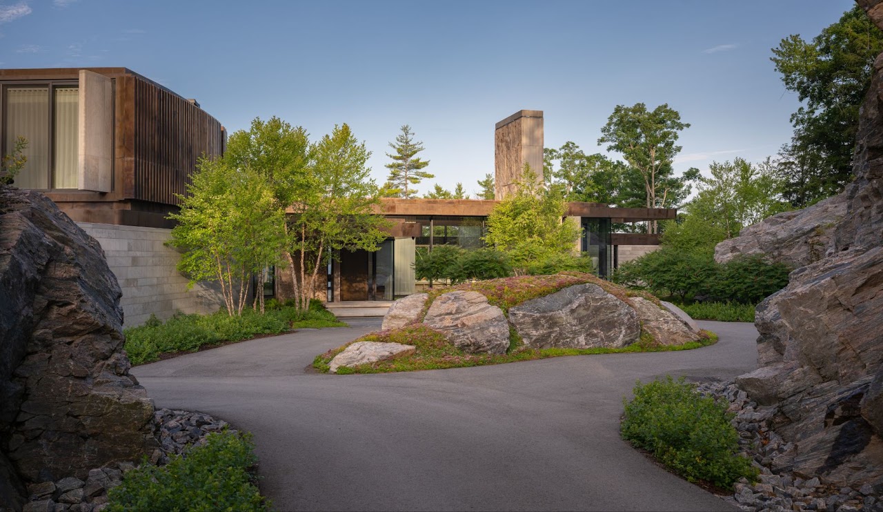natural stone and trees in front of a house with a circular path