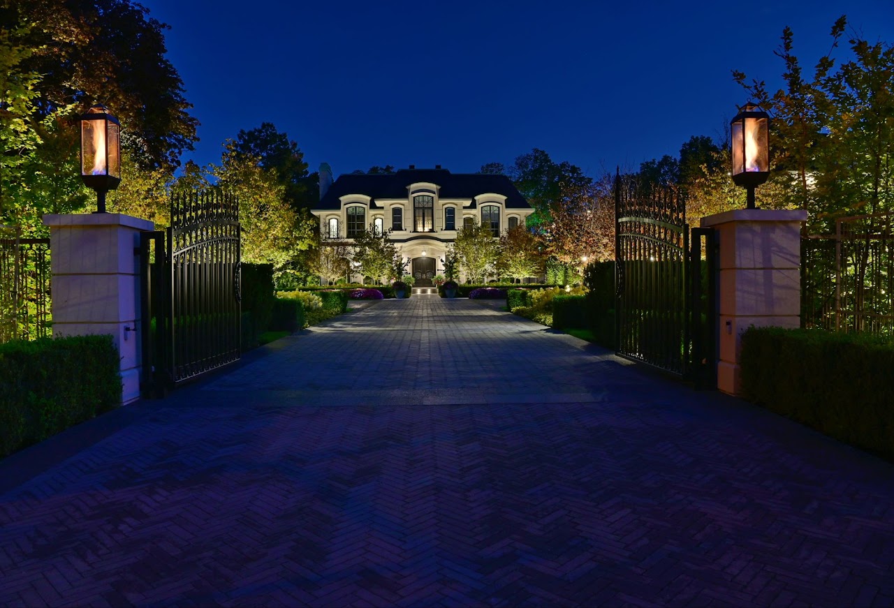 large house lit up at night at the end of a long driveway with open gates