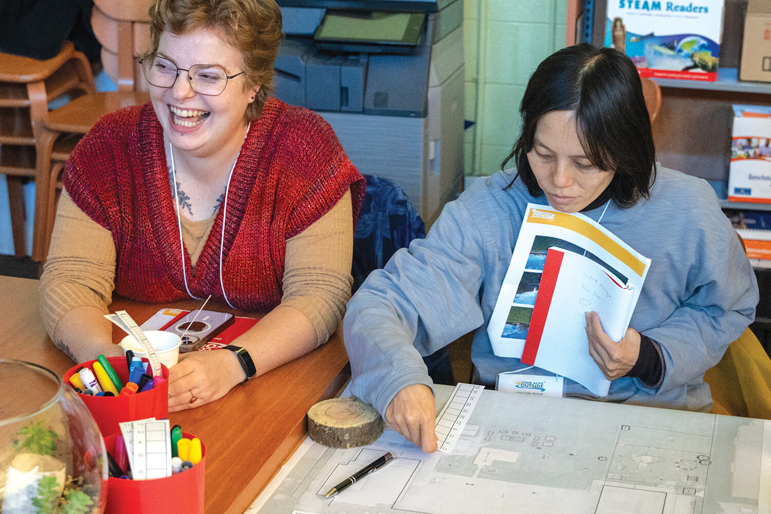two women sitting at a table with one laughing