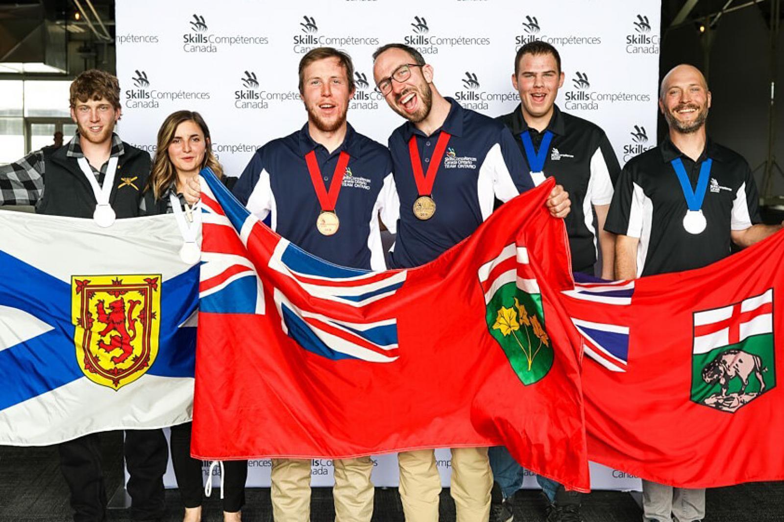 Thomas Hawley and Blaise Mombourguette (centre) hold the Ontario flag at the Skills Canada winners podium.